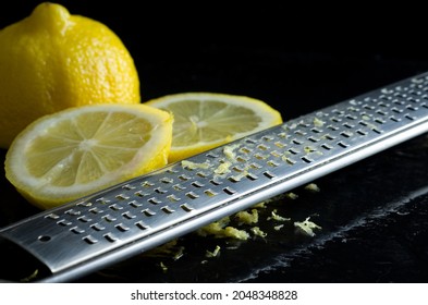 Macro Image Of Cheese Grater With Fresh Lemons And Lemon Zest On Wet Black Kitchen Counter Horizontal