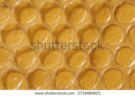 Macro image of clear plastic bubble wrap overlaying Yellow textured paperboard, showing air-filled circles and surface creases.