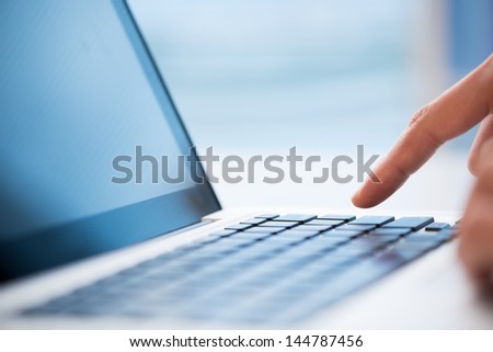 Macro image of a finger being about to press a key on a laptop keyboard