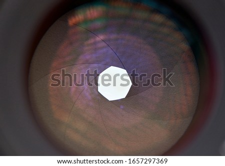 A macro image of the inside of a camera lens, showing the aperture and it's rings or blades, with a white background.                                     