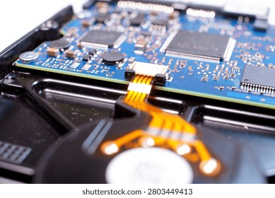 Macro image of the internal device of a hard disk (HDD). A part of the rotating spindle with discs is visible at the bottom of the frame and a blue control circuit board located above it. 
