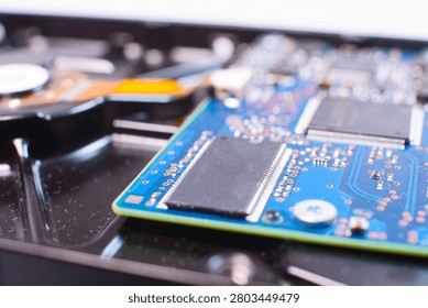 Macro image of the internal device of a hard disk (HDD). A part of the rotating spindle with discs is visible at the bottom of the frame and a blue control circuit board located above it. 