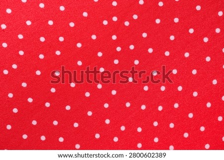 Macro image of red fabric featuring an evenly spaced white polka dot pattern and smooth textile surface.