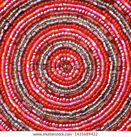 Macro image of small shiny iridescent pink glass beads sewn in a pattern of concentric circles. 