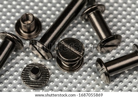 A Macro image of various sized Chicago Screws or Barrel Bolts of varying lengths on a stainless steel industrial background.