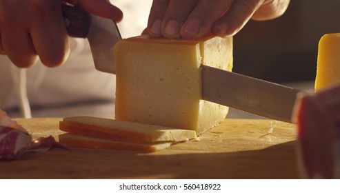  Macro Of A Middle Aged Chef Cutting Cheese With Knife On Wooden Board On Restaurant Kitchen Table (extra Close Up)