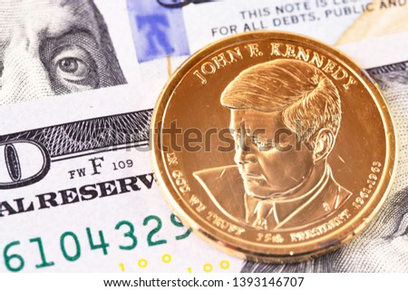 macro one dollar golden coin with John F. Kennedy portrait, and hundred dollars banknotes
