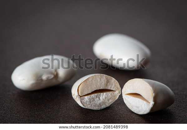 Macro photo of 3 lima beans, one divided in\
half. All over a dark brown\
surface.
