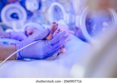 Macro photo of doctor's hands and legs of a child. Newborn is placed in a medical incubator under ultraviolet lamp. Neonatal intensive care unit.