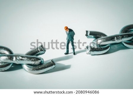 Macro photo of thoughtful businessman figurine standing between broken chain.  Sad and stressed miniature man close-up. Sad and stressed miniature man close-up. Conflict, bankruptcy, uncertainty.