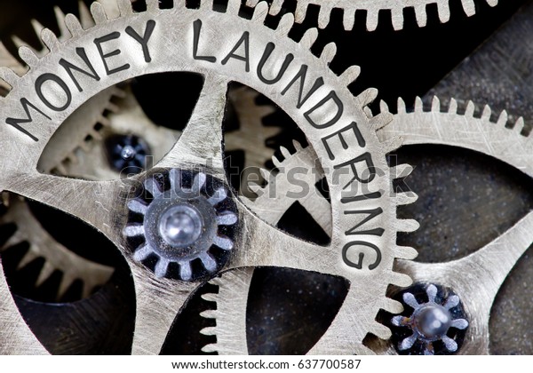 Macro photo of tooth wheel\
mechanism with MONEY LAUNDERING letters imprinted on metal\
surface