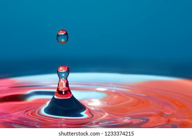 Macro photo of water drops falling into a pool of water, causing a splash and ripples. High speed flash photography technique used to freeze the action. Colorful background includes blues and pinks. - Powered by Shutterstock