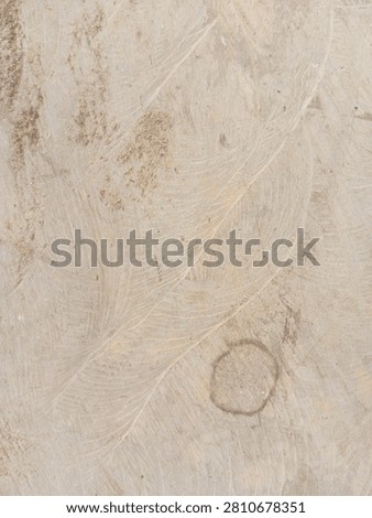 A macro photograph capturing the dynamic and weathered topography of a raw, light-colored industrial surface. The structural composition is defined by prominent, sweeping curvilinear brush or sanding patterns that form a delicate, fan-like lattice deeply engraved across the plane. A distinct, dark circular ring stain anchors the lower-right quadrant, providing a stark narrative of utility and imperfection alongside scattered patches of fine sand, dirt particles, and mineral residue along the left margins. The neutral color palette features a base of pale beige, soft cream, and light tan, contrasted by the earthy brown tones of the organic debris and ring blemish. This high-resolution asset is ideal for commercial use as a rustic texturized backdrop, a 3D material overlay for architectural rendering, or a background for industrial and wabi-sabi inspired branding portfolios. The raw, unpolished, and scarred physical finish delivers a powerful psychological impact of rugged grounding, raw authenticity, endurance, and permanent structure.