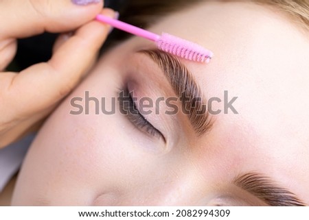 macro photography of the model's hairs the master combs the eyebrow hairs with a pink brush after the procedure long-term styling and lamination Foto stock © 