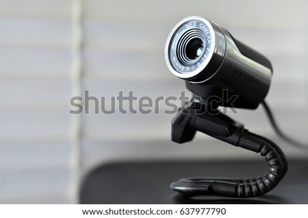 Macro photography of a wired web camera for stationary computers and laptops. A web camera image of a cylindrical shape lying on the computer surface. Focus on the camera lens