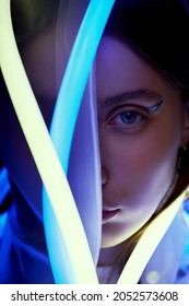 Macro Portrait Of Mystic Woman In White Transparent Raincoat And Flexible Blue And Yellow Neon Tube Light. Black Background                                         