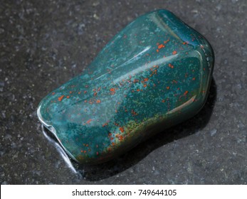 macro shooting of natural mineral rock specimen - polished green Heliotrope (bloodstone) gem stone on dark granite background from India