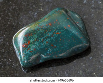 macro shooting of natural mineral rock specimen - tumbled green Heliotrope (bloodstone) gem stone on dark granite background from India