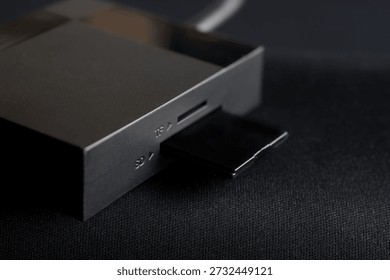 Macro shot of a black SD memory card inserted into a reader slot on a dark textured surface. Digital data storage and backup concept. Photo