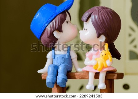 Macro shot of boy and girl dolls. These cute adorable toys are less than 5 cm long. They're very detail. In the picture the boy and the girl stand on a flat bench representing the love.