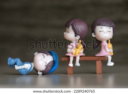 Macro shot of boy and girls dolls. These cute adorable toys are less than 5 cm long. They're very detail. In the picture, two girls stand on a flat bench, while the boy is laid on the ground. 