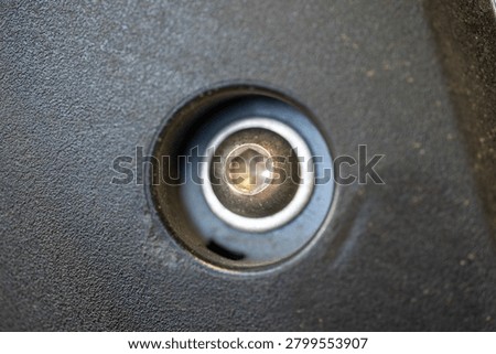 A macro shot captures a metallic hex socket head cap screw deeply recessed within a dark, textured surface. The hexagonal indentation of the screw head is visible, reflecting light against the gritty background material.