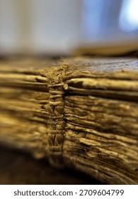A macro shot capturing the intricate, rustic detail of an antique book's spine and aged paper edges. The image powerfully conveys a sense of history and timeless knowledge