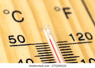 A macro shot of a classic wooden thermometer showing a temperature over 50 degrees Celsius, 122 degrees Fahrenheit.