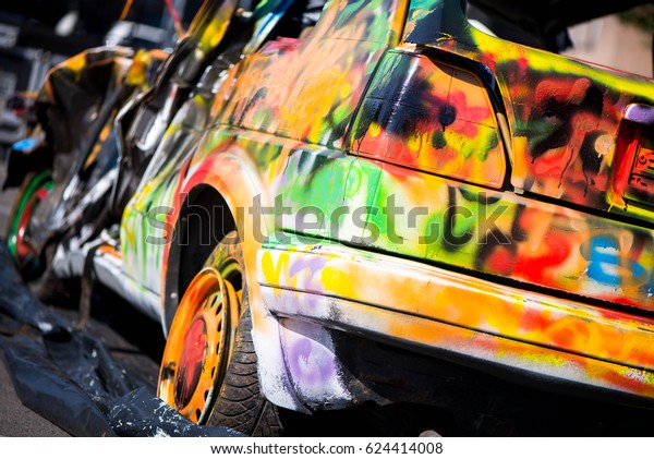 Macro shot of a colorfully painted car, an old\
crashed, damaged car wreck. Kids are having fun, making drawings\
and graffiti art, paint on wreck and tires with green, red, orange,\
yellow, blue colors.