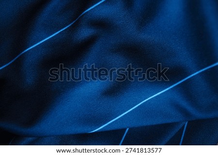 Macro shot of dark blue technical performance fabric. Detailed view of synthetic textile with elegant pinstripes and dramatic fluid folds. High-quality jersey knit material for professional football kits and luxury activewear design.