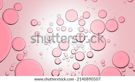 Macro shot of different sized rose oil bubles float in clear liquid against pale pink background | Abstract skin care formulation concept background