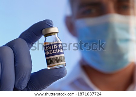 Macro shot of a doctor wearing face mask and latex gloves demonstrating the new covid-19 vaccine in vial. Close up portrait, copy space, background.