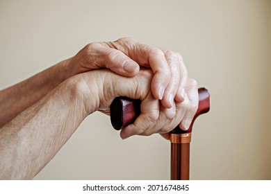 Imagen de macro de las manos de una anciana sosteniendo la manilla de madera de un bastón de caminar. Cerrar, copiar espacio para texto, fondo neutro.