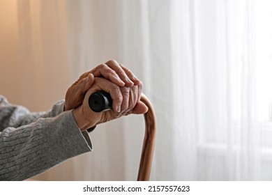 Macro Shot Of Elderly Woman's Hands Holding The Wooden Handle Of A Metal Walking Cane. Close Up, Copy Space For Text, Background.