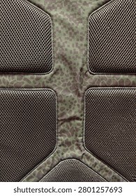 A macro shot of an ergonomic backpack back panel featuring breathable air mesh padded cushions and a green camouflage animal print textile design