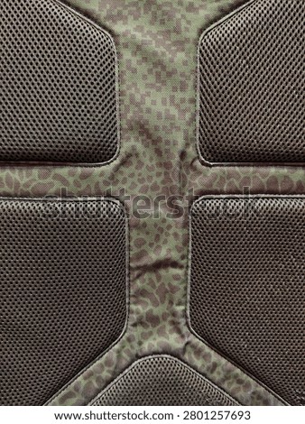 A macro shot of an ergonomic backpack back panel featuring breathable air mesh padded cushions and a green camouflage animal print textile design
