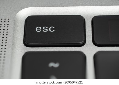 Macro shot of an Esc (escape) button on a black laptop keyboard with a silver metallic background 