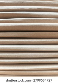 Macro shot featuring a neat stack of corrugated cardboard sheets in creamy brown tones arranged horizontally. Each layer displays a rough yet natural paper fiber texture, with soft shadows between the stacks creating visual depth and a soothing repetitive line pattern. Natural lighting highlights the recycled material surface details and warm earthy nuances. Perfect for eco friendly packaging concepts, paper industry themes, minimalist abstract backgrounds, or sustainability illustrations.