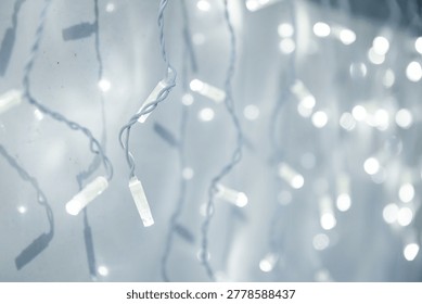 Macro shot of glowing white string fairy lights shaped like icicles. Christmas holiday decoration and festive led illumination background.