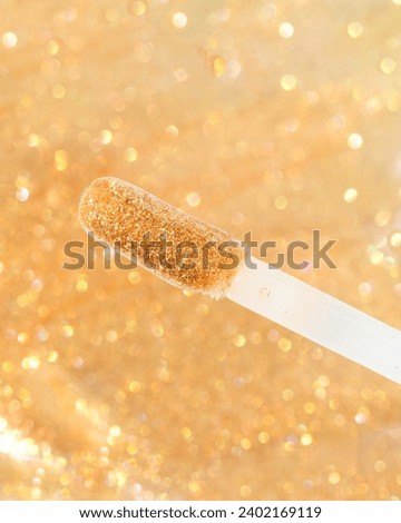 Macro shot of gold glitter lipgloss on doe foot applicator with lipgloss background 