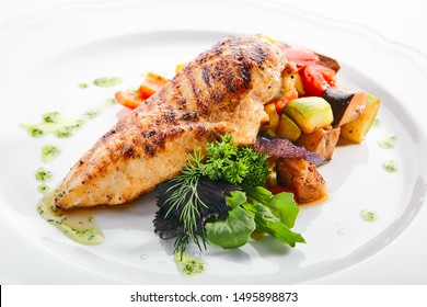 Macro shot of grilled chicken fillet with side dish of baked vegetables on white restaurant plate isolated. Bbq chicken breasts or white meat barbecue with fried zucchini and bell pepper closeup