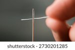 Macro shot of a hand threading white thread through an eye of needle. Symbol of precision, patience, and handmade craft concept 
