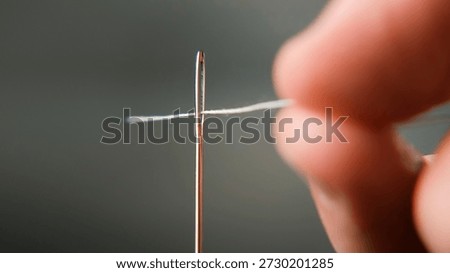 Macro shot of a hand threading white thread through an eye of needle. Symbol of precision, patience, and handmade craft concept 