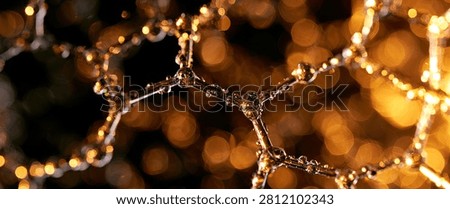 Macro shot of a hexagonal molecular lattice, possibly graphene, adorned with tiny water droplets, set against a blurred background of warm, golden bokeh lights.