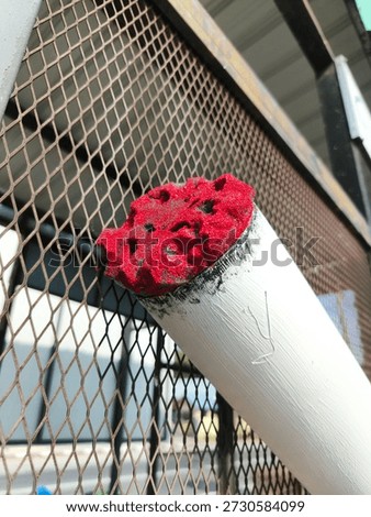 A macro shot of a large scale cigarette art installation featuring a textured red cherry tip and white body against a metal mesh background