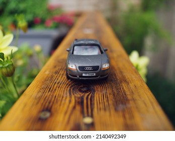 Macro shot of miniature Audi car model on garden decking fence, sorrounded by foliage