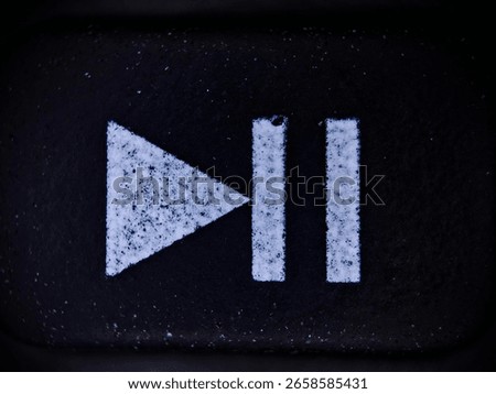 A macro shot of a play-pause button, featuring textured white symbols against a black background. The image highlights the contrast and detail of the button's surface.