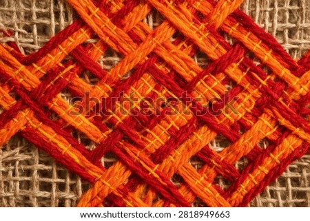 Macro shot of red and orange thread interwoven on burlap with material, handmade