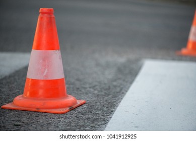 Macro shot of road traffic cones with orange and white stripes standing on street on gray asphalt during road construction works. Just painted white street lines on pedestrian crossing - Powered by Shutterstock