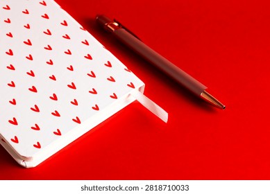 Macro shot of a section of a white notebook with a heart pattern and a premium pen, capturing the paper texture on a flat red background.